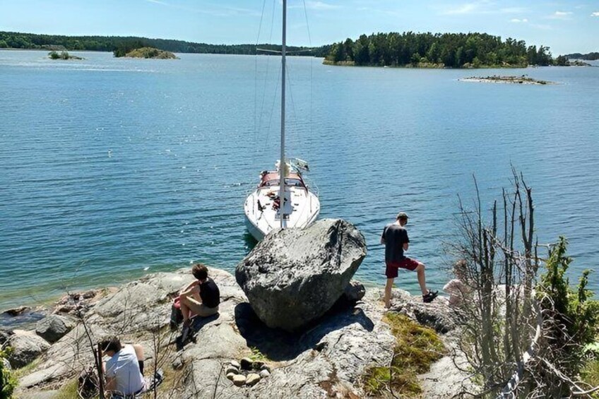 A sailboat on calm water, a large rock, and a person standing on the shore. 5