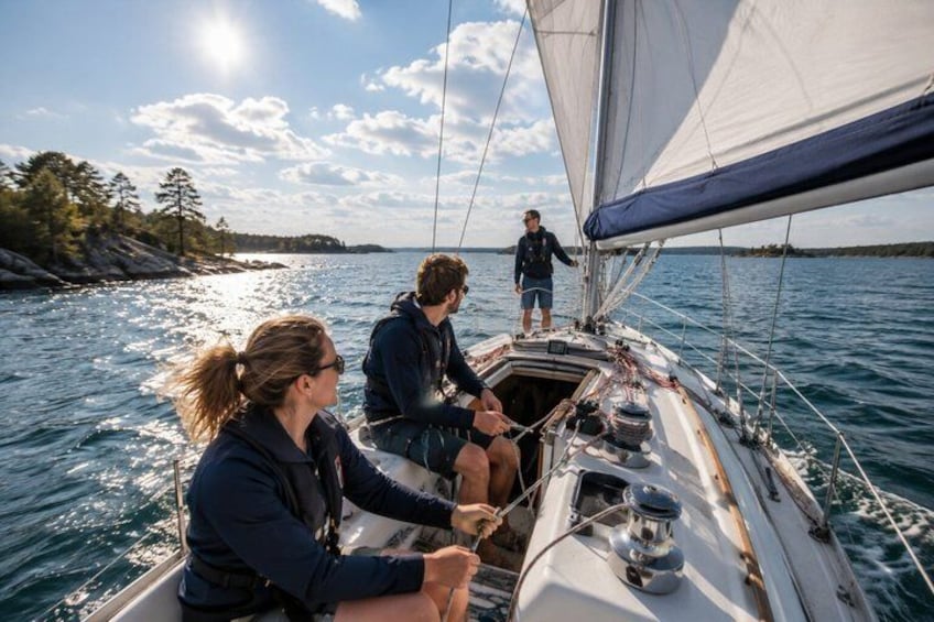 A sailboat on calm waters with a person standing at the stern and another person steering. 1