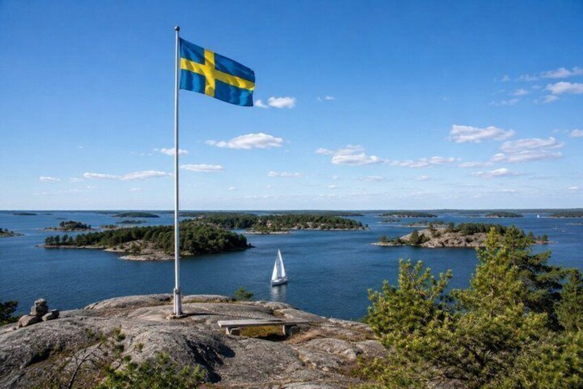A flag on a rock, a sailboat, and a body of water with islands. 2