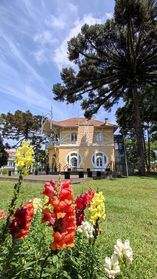 A building with a yellow facade and white trim, surrounded by a grassy area with colorful flowers. 5