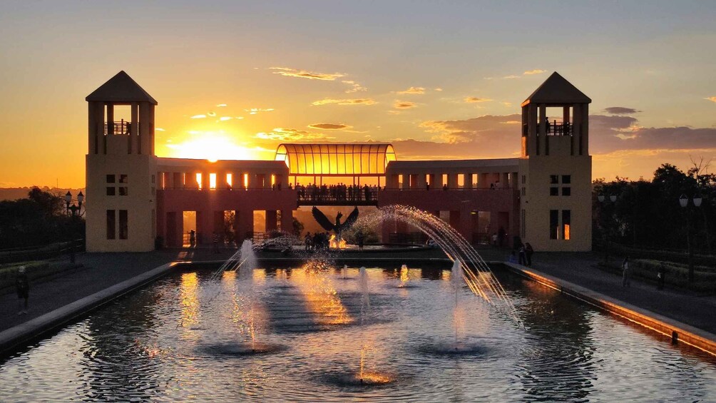 A sunset over a historic building with two towers and a fountain in the foreground. 1