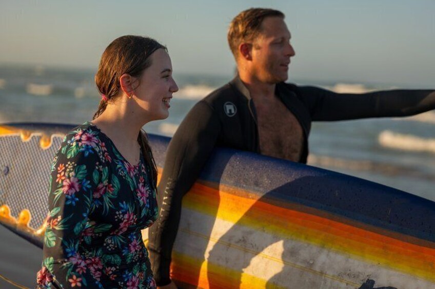 Two people holding a colorful surfboard at the beach. 3
