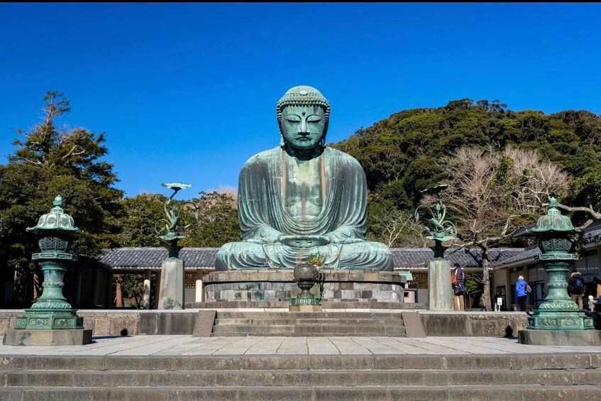 A large seated Buddha statue in a temple courtyard with steps leading up to it, surrounded by traditional Japanese architecture and greenery. 1