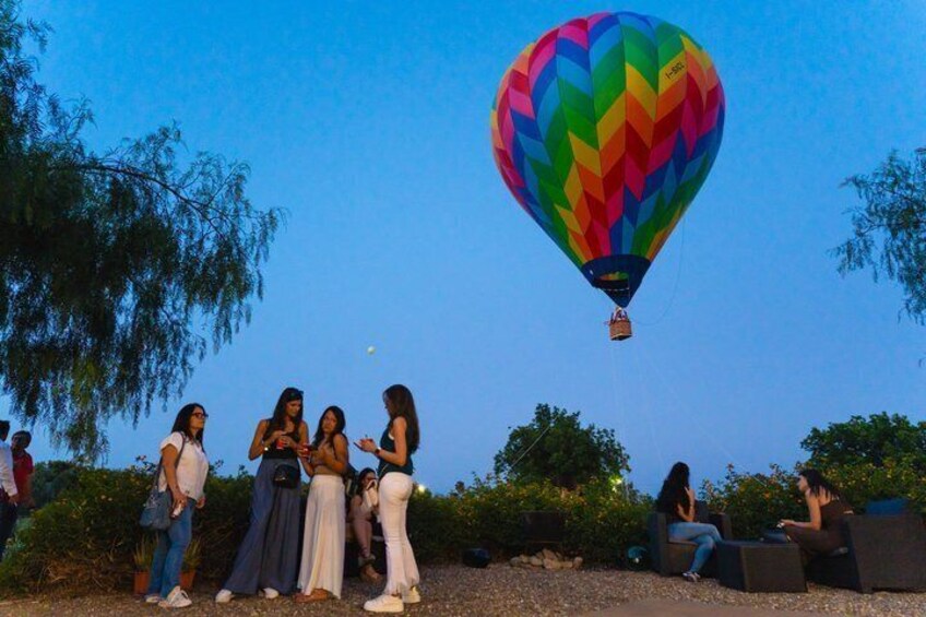 A group of people gathered outdoors, a colorful hot air balloon in the sky, and a clear blue sky. 2