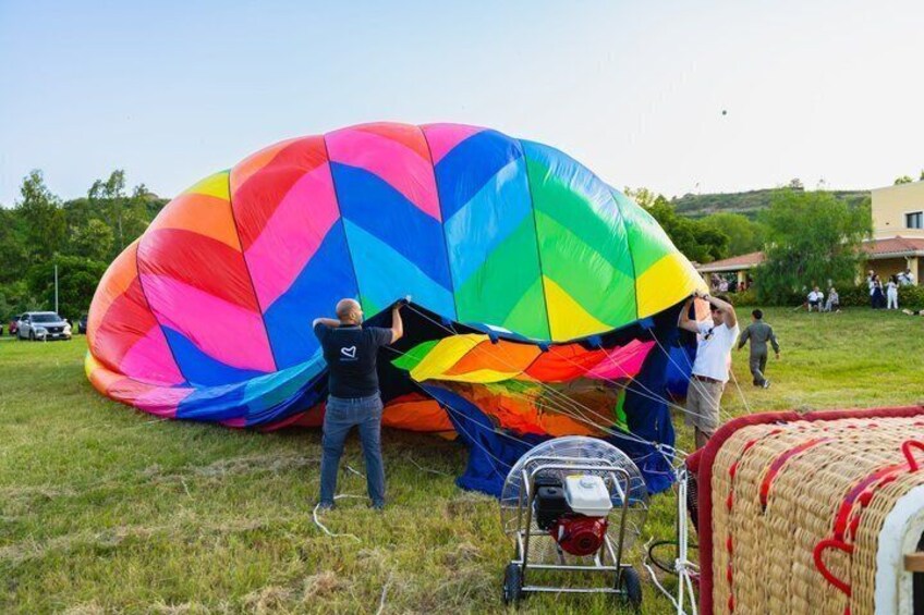 A colorful hot air balloon being inflated on a grassy field with a few people and a house in the background. 3