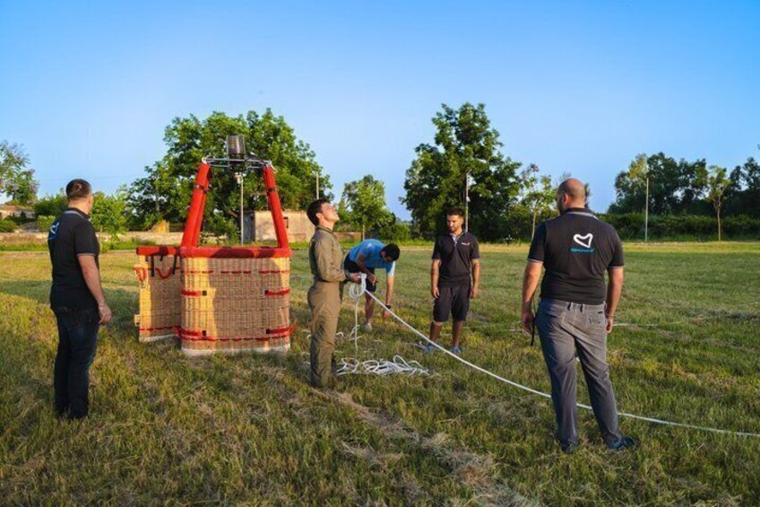 A group of people around a large, red and beige structure in an open field. 4