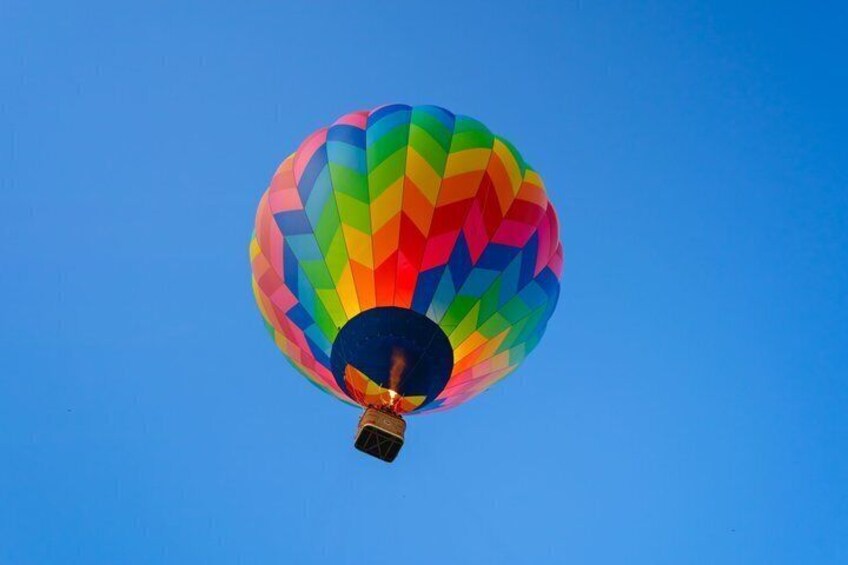 A hot air balloon with a rainbow pattern against a clear blue sky. 1