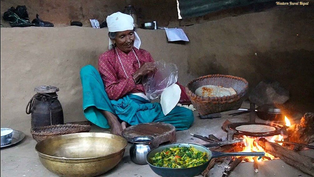 A person cooking outdoors with a fire, surrounded by cooking utensils and food. 1