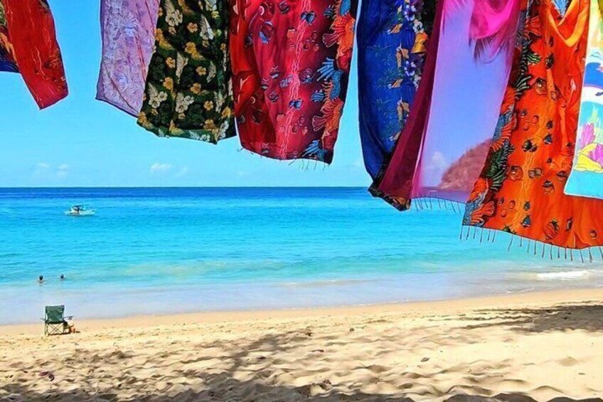 A beach with colorful fabrics hanging, a clear blue sea, and a single person in the distance. 5