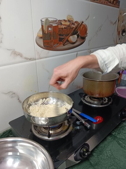 A person cooking, with a bowl of flour on a stove and a pot on the side. 5