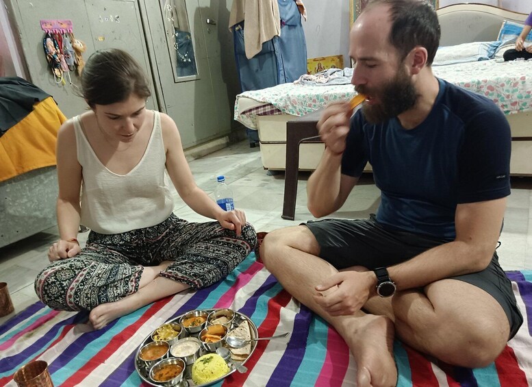 Two people sitting on a striped mat with a meal in front of them. 3