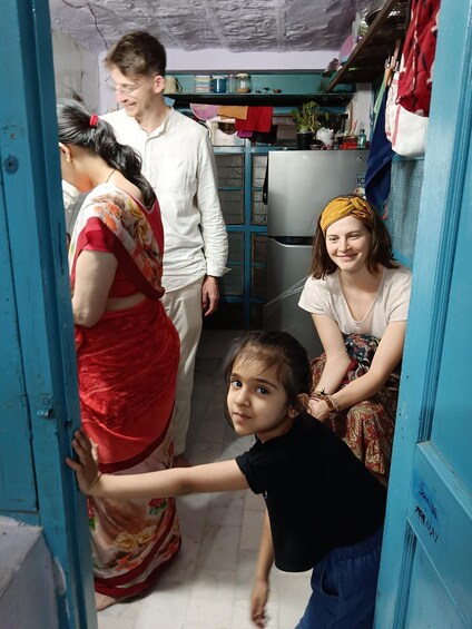 A family in a narrow room with blue walls, a refrigerator, and shelves with various items. 2