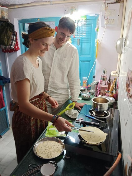 Two people cooking in a kitchen with a stove, utensils, and a pot on the counter. 1