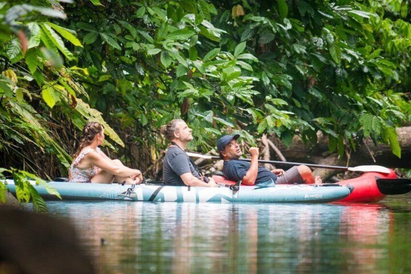 Three people in a blue inflatable raft on a calm river surrounded by dense green foliage. 3