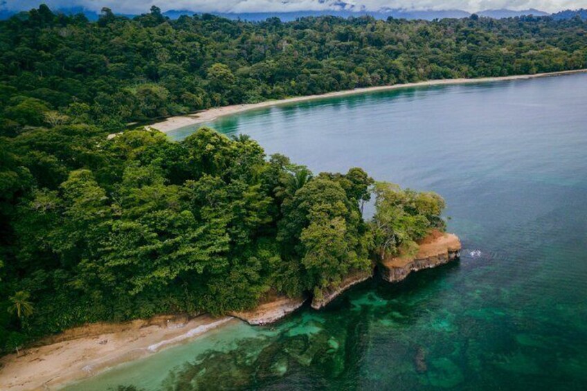 A coastal landscape with dense forest, clear turquoise waters, and a sandy beach. 2