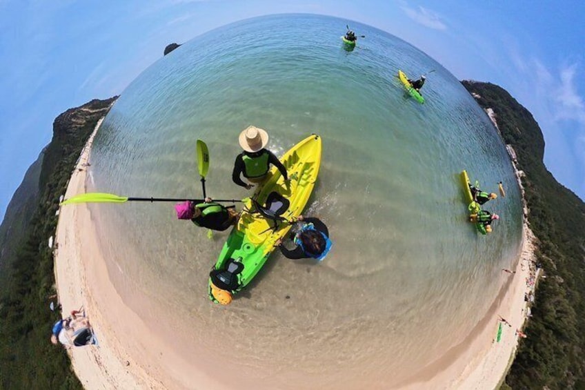 A beach with kayakers in green and yellow kayaks, a clear sky, and a calm sea. 1