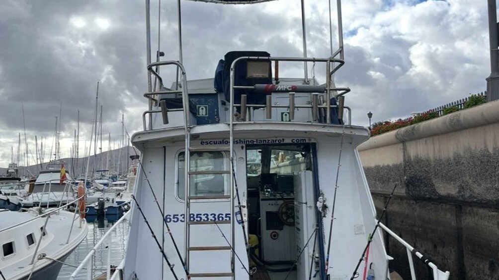 A boat docked at a marina with other boats, a cloudy sky, and a concrete wall with vegetation. 3