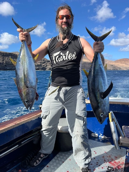 A person holding two fish on a boat with a rocky coastline in the background. 1