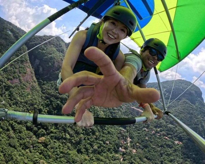 Two people in a tandem hang glider with a mountainous landscape in the background. 2