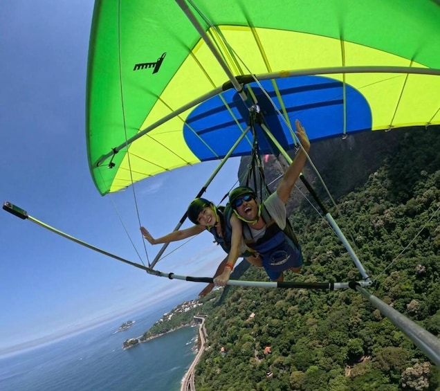 Two people paragliding over a coastal area with dense greenery and a clear view of the sea. 1
