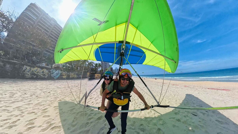 A person parasailing on a beach with a green canopy, a clear sky, and a distant shoreline. 3