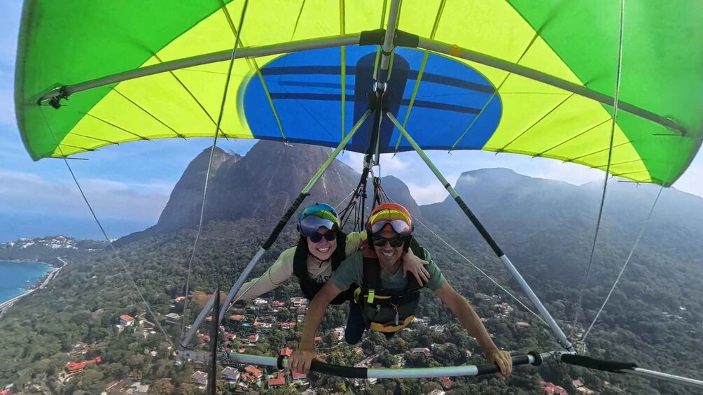 Two people paragliding with a mountainous landscape and a coastline in the background. 2