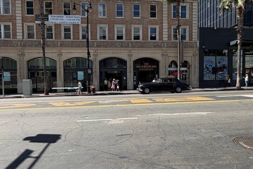 A street corner with a black car, pedestrians, and a building with 'The Hollywood Experience' sign. 3