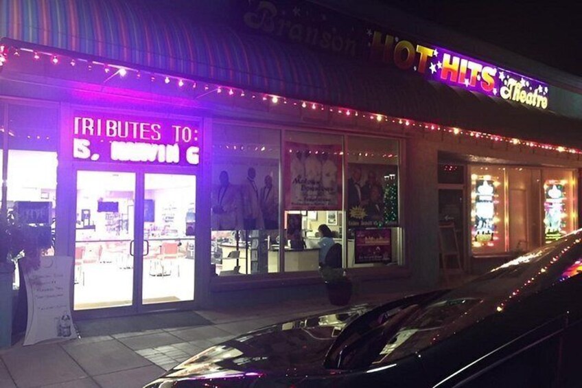 A brightly lit storefront with neon signs, including one that reads 'HOT HITS Theater.' 2