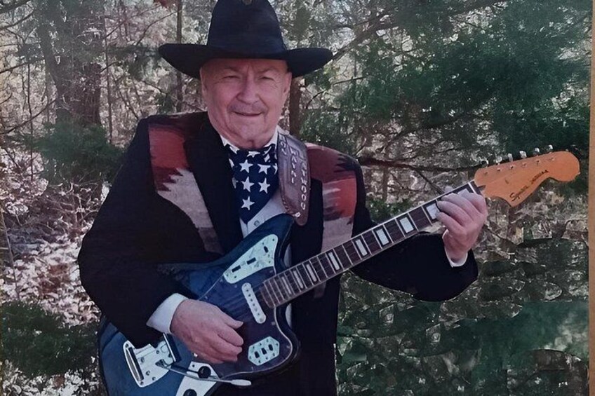 A person playing an electric guitar outdoors with trees in the background. 2
