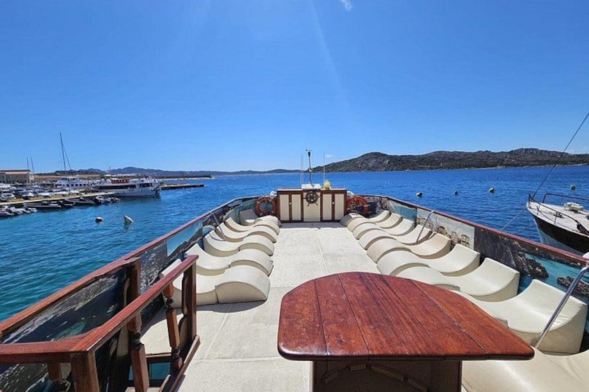A boat deck with seating and a table, surrounded by calm water and other boats. 3