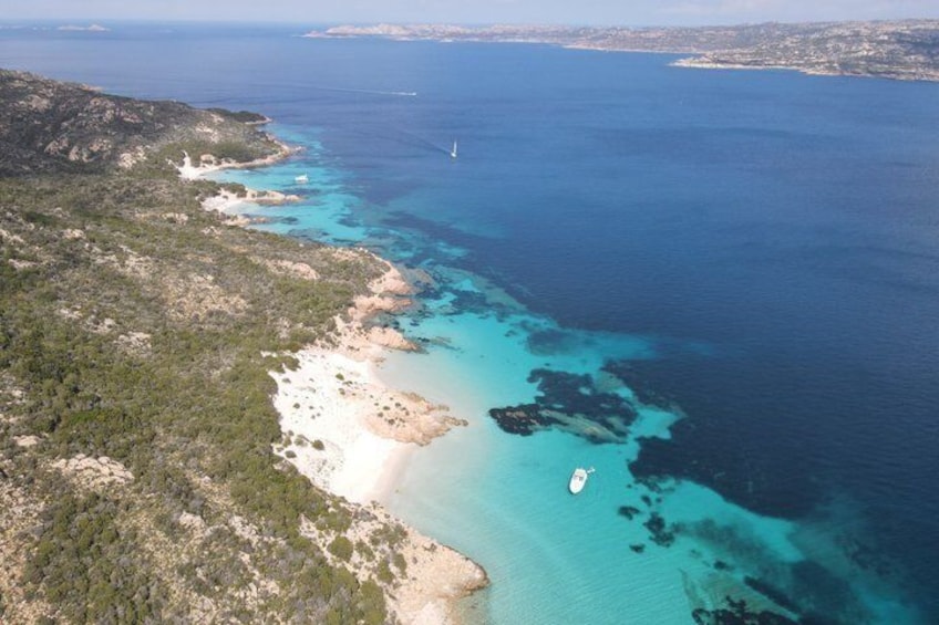 A coastal landscape with a sandy beach, clear turquoise waters, and rocky outcrops. 5