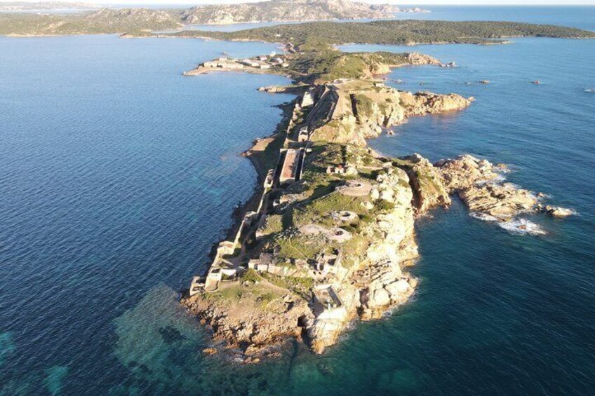 An aerial view of a coastal island with a fortified structure, clear blue waters, and rocky terrain. 1