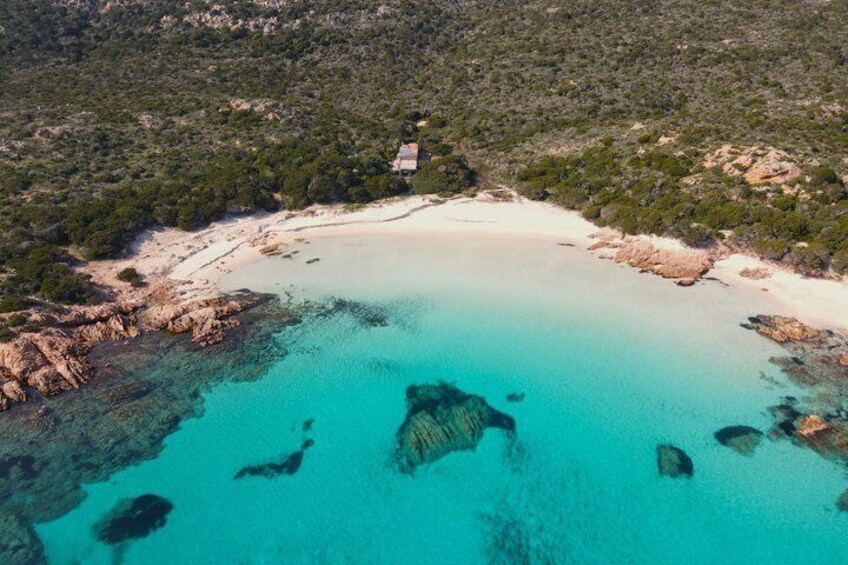 A coastal landscape with clear turquoise waters, rocky outcrops, and a small building on a sandy beach. 3
