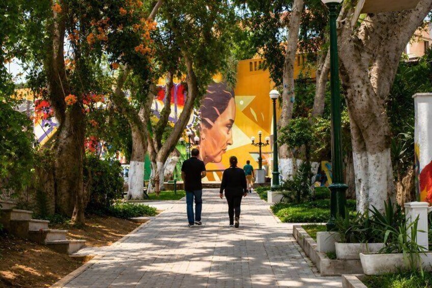 A tree-lined pathway with a mural in the background. 2