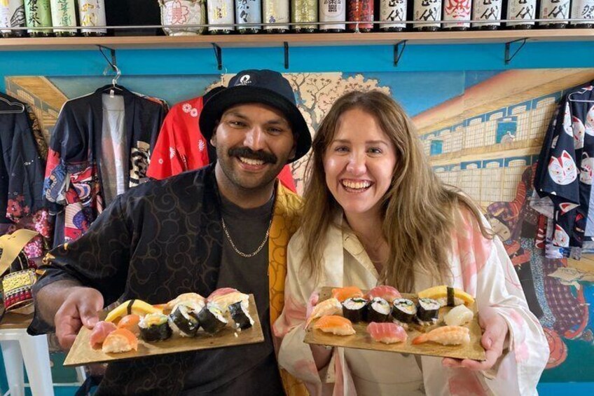 Two people holding plates of sushi in a store with clothing and artwork in the background. 2