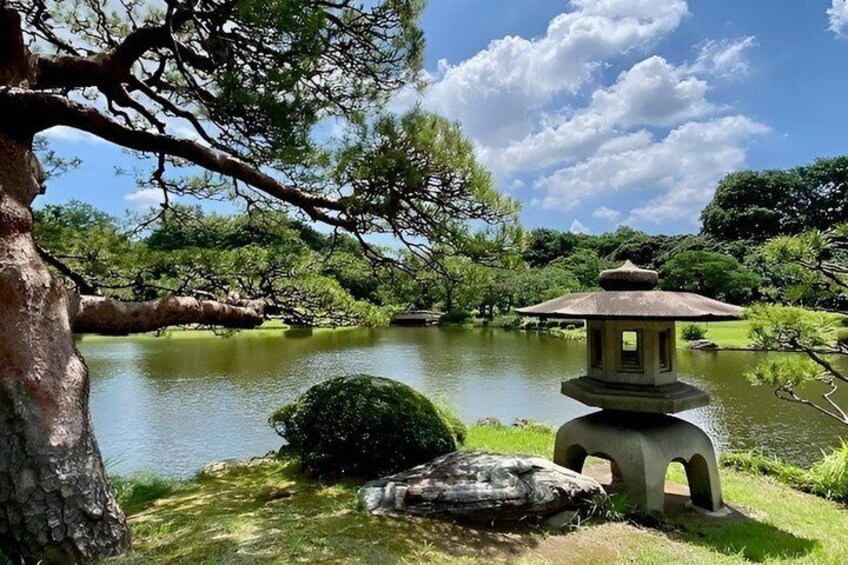 A serene pond with a traditional Japanese lantern, lush greenery, and a large tree. 4