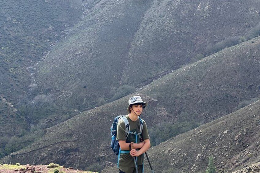 A person standing on a mountain ridge with a backpack and hiking poles, surrounded by steep, rocky terrain. 2
