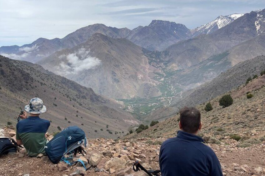 Two people sitting on a rocky hillside overlooking a valley with mountains in the distance. 3
