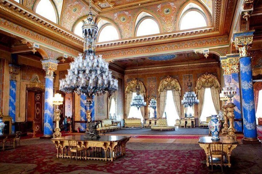 An opulent room with ornate chandeliers, blue and gold columns, and a red carpet. 4