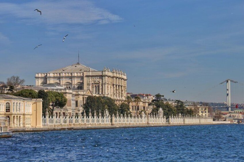A historic building by a waterfront with a white fence and birds in the sky. 2