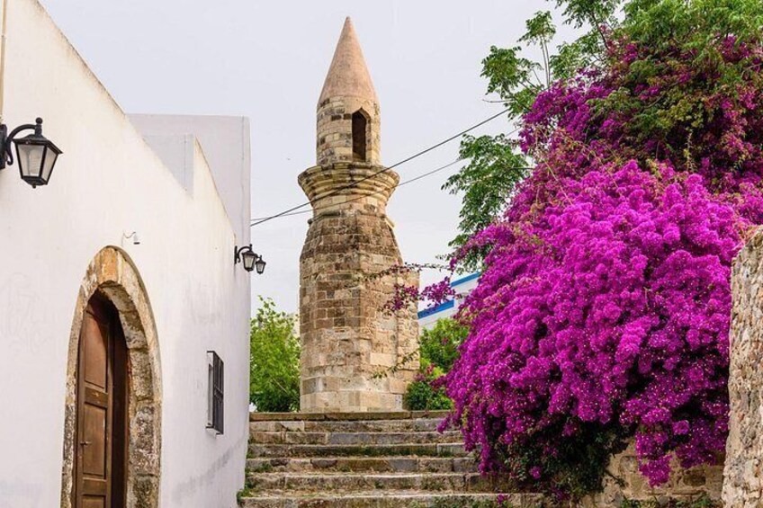 A white building with a wooden door, a stone tower, and purple bougainvillea flowers. 2