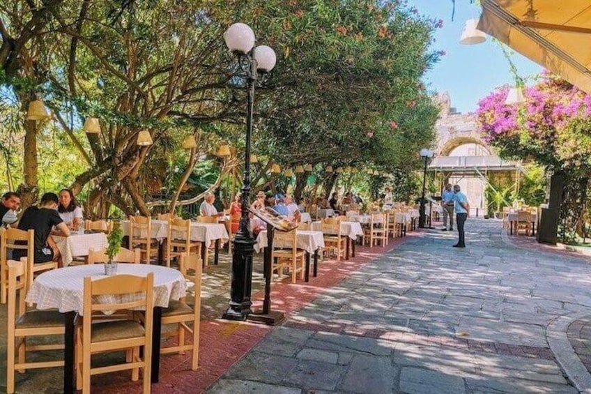 An outdoor restaurant with wooden tables and chairs, surrounded by trees and flowers. 3