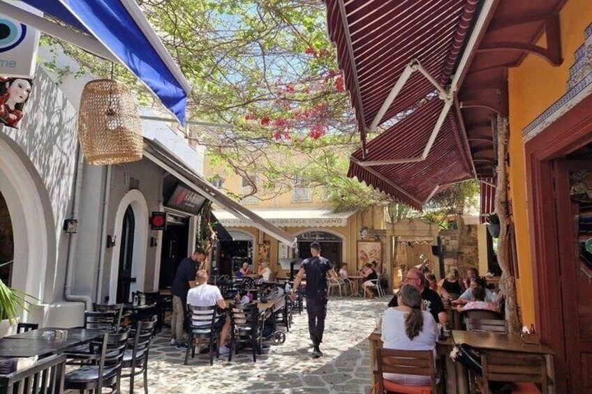 A cobblestone street with outdoor seating, a waiter walking, and people dining. 4