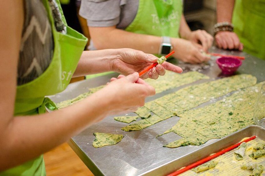 People preparing food, specifically cutting dough on a metal surface. 1