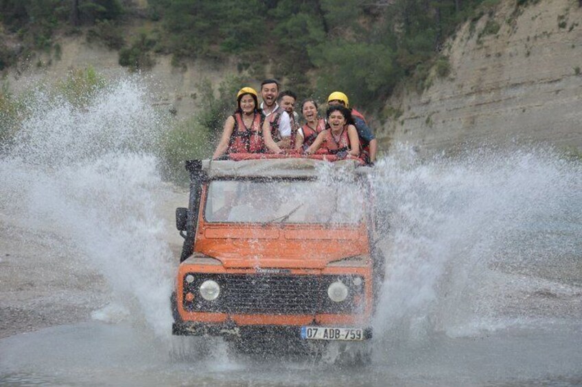 A group of people in a vehicle driving through a water body, splashing water around. 1