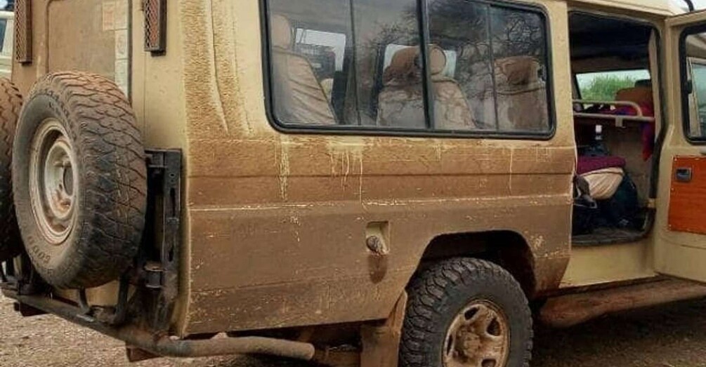 A dirty, beige off-road vehicle with a spare tire mounted on the back, and a door open revealing a person inside. 3