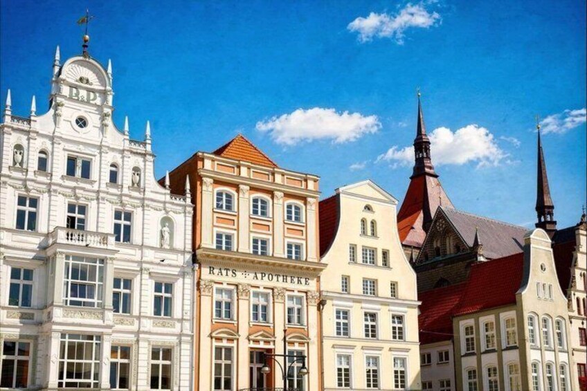 A row of historic buildings with varied architectural styles, including a prominent white building with a clock tower and a building with a sign that reads 'RATS APOTHEKE.' 3