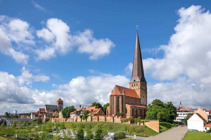 A church with a tall spire, a red-roofed building, and a small white structure in a town square. 4