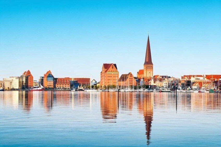 A calm waterfront cityscape with historic buildings and a prominent church spire. 1