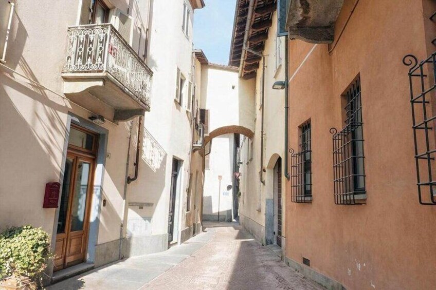 A narrow street with buildings on either side, a wooden door, and a balcony with a wrought iron railing. 2